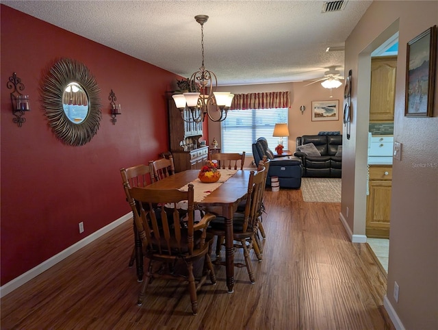 dining area featuring ceiling fan with notable chandelier, a textured ceiling, baseboards, and wood finished floors