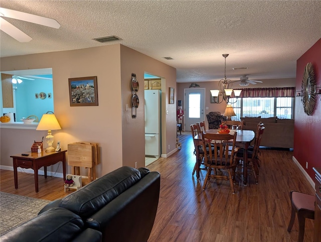 dining space featuring a textured ceiling, visible vents, baseboards, wood finished floors, and ceiling fan with notable chandelier