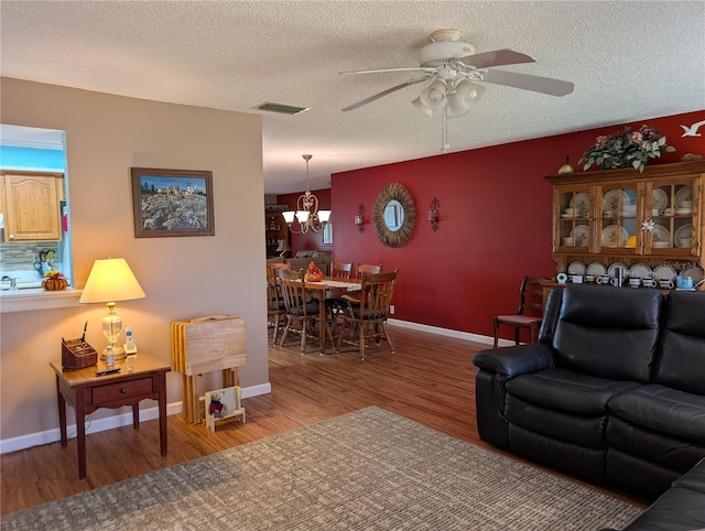 living area featuring ceiling fan with notable chandelier, visible vents, wood finished floors, and a textured ceiling