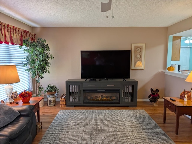 living room featuring wood finished floors, a textured ceiling, baseboards, and ceiling fan