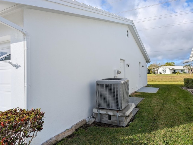 view of side of property featuring stucco siding, central AC, and a yard