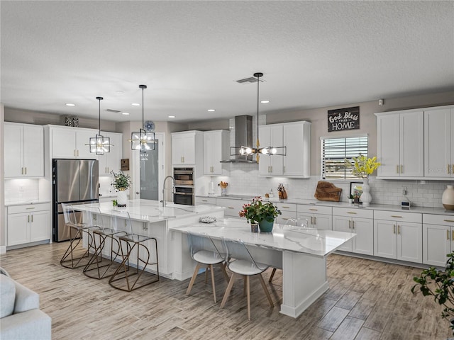 12808 Boggy Creek Dr, Riverview, FL 33579 - kitchen with a notable chandelier, a large island with sink, a kitchen breakfast bar, appliances with stainless steel finishes, and wall chimney range hood