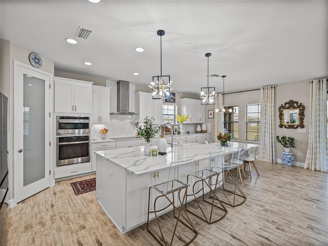 12808 Boggy Creek Dr, Riverview, FL 33579 - kitchen with black electric stovetop, wall chimney exhaust hood, light wood-style floors, and a kitchen bar
