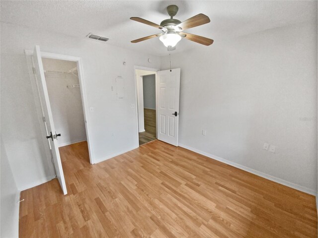 unfurnished bedroom featuring baseboards, visible vents, light wood-style flooring, a closet, and a walk in closet
