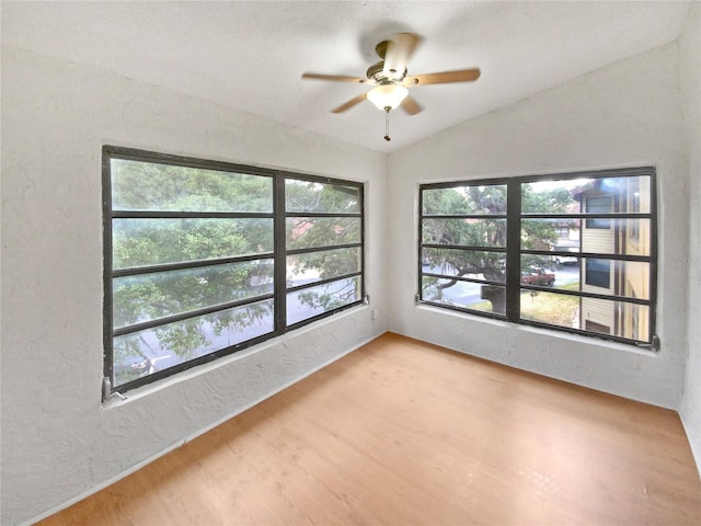 spare room featuring light wood finished floors, lofted ceiling, a ceiling fan, and a textured wall