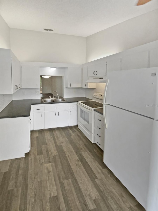 kitchen featuring visible vents, a sink, under cabinet range hood, dark countertops, and white appliances