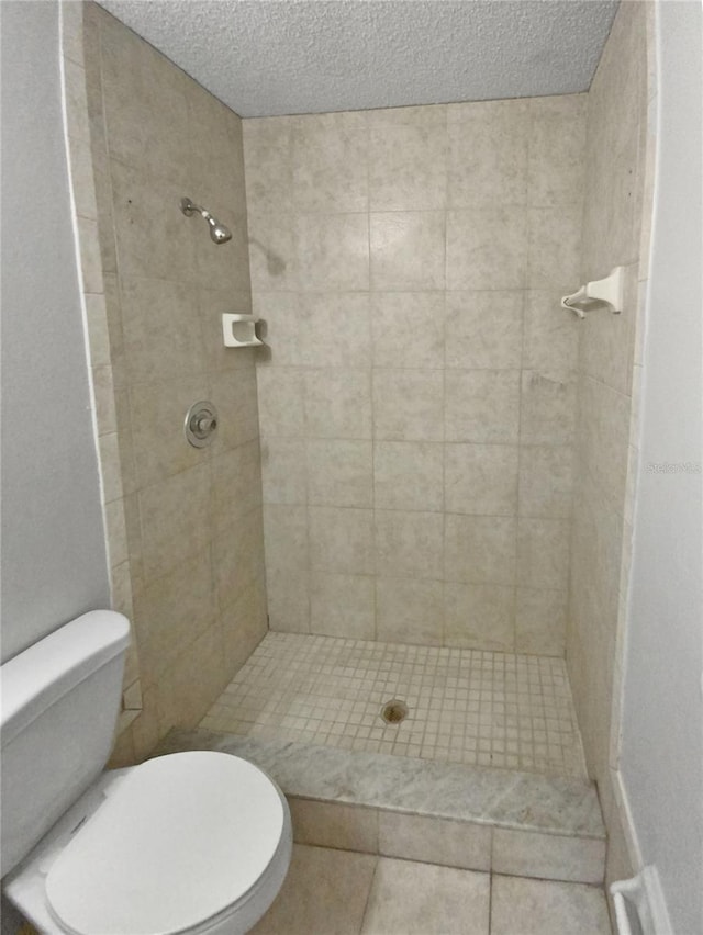 bathroom featuring toilet, a tile shower, and a textured ceiling