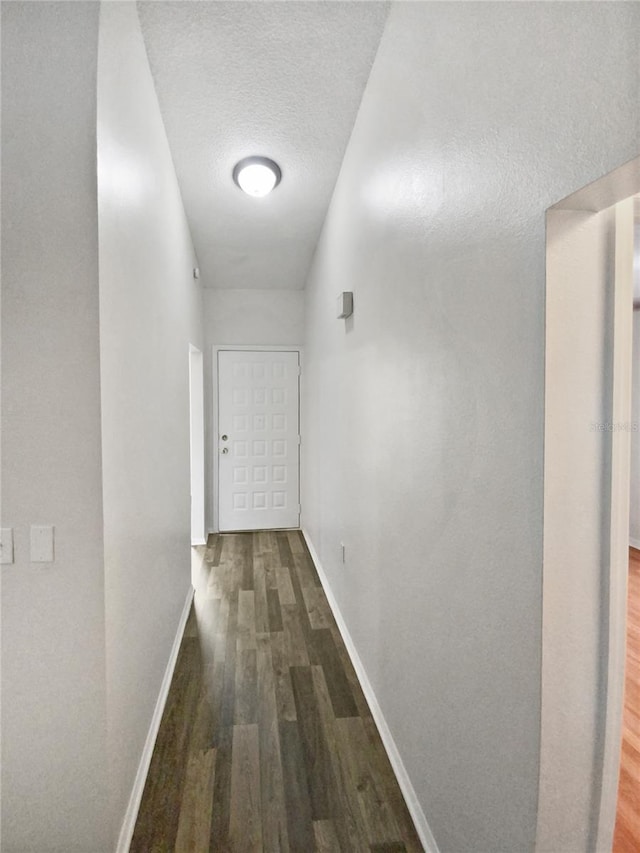 hall featuring a textured ceiling, baseboards, and wood finished floors