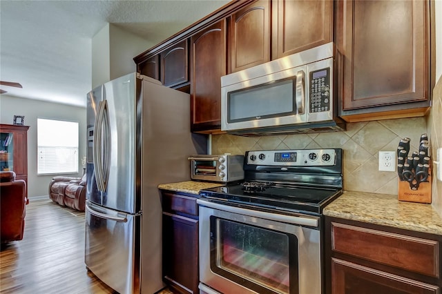 4250 Warwick Hills Dr, Wesley Chapel, FL 33543 - kitchen with appliances with stainless steel finishes, light stone counters, backsplash, wood finished floors, and open floor plan