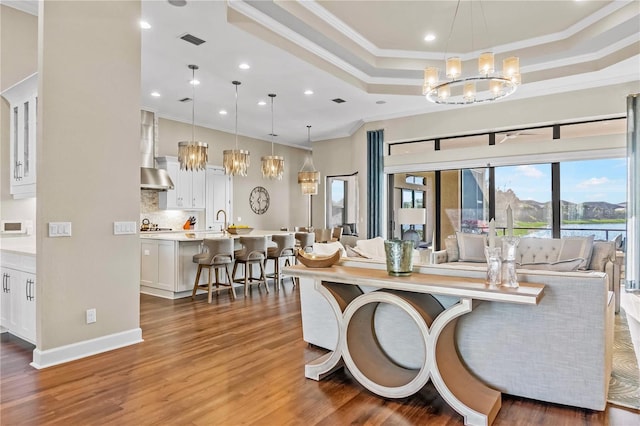 living room featuring ornamental molding, a raised ceiling, visible vents, a notable chandelier, and wood finished floors