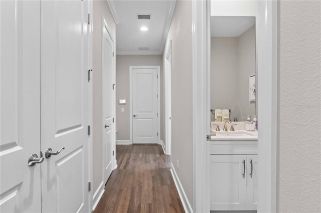 corridor featuring recessed lighting, ornamental molding, baseboards, a sink, and dark wood-style floors