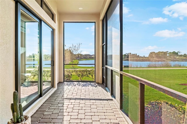unfurnished sunroom with a water view, a wealth of natural light, and brick floor