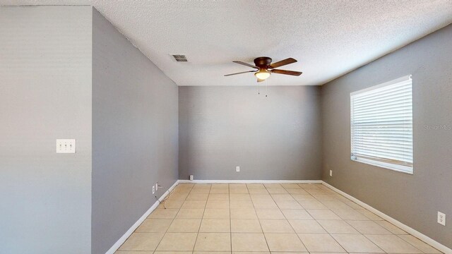 spare room featuring light tile patterned floors, a ceiling fan, visible vents, baseboards, and a textured ceiling