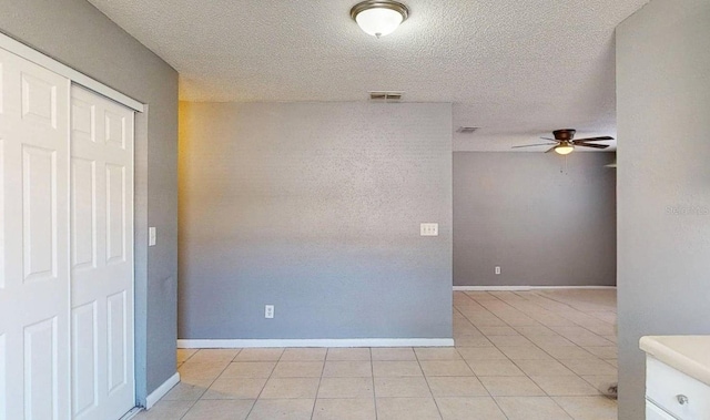 spare room with a textured ceiling, a ceiling fan, visible vents, and baseboards