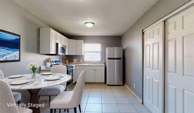 kitchen featuring light tile patterned floors, a sink, light countertops, white cabinets, and appliances with stainless steel finishes
