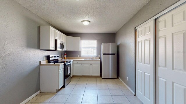 kitchen featuring a sink, stainless steel appliances, light countertops, white cabinetry, and a textured wall