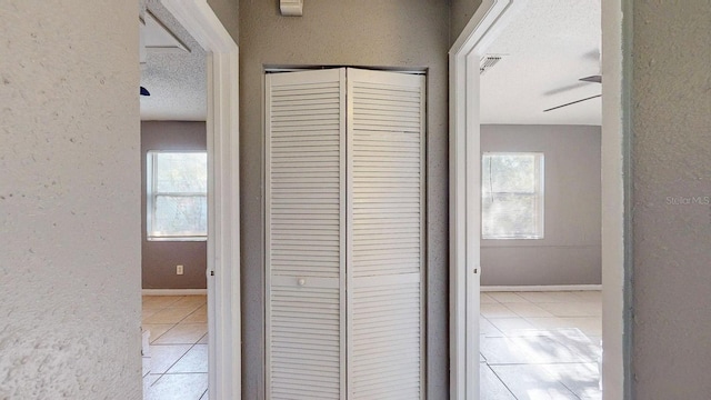 hall featuring light tile patterned floors, a textured ceiling, a wealth of natural light, and a textured wall