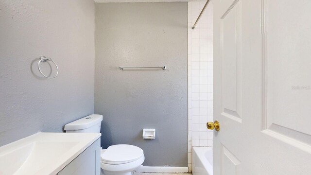 full bath with vanity, baseboards, tub / shower combination, toilet, and a textured wall
