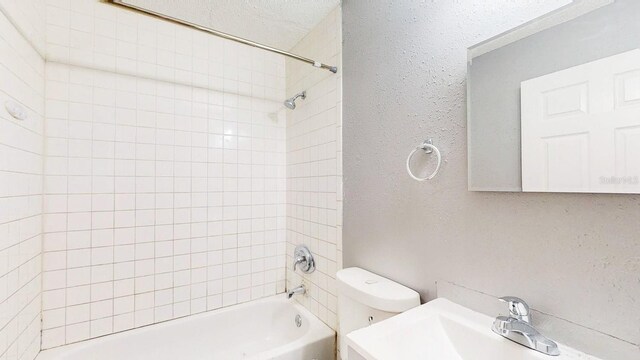 full bathroom featuring toilet, shower / tub combination, a textured wall, and a sink