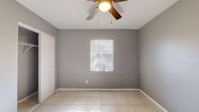 unfurnished bedroom featuring light tile patterned floors, a closet, baseboards, and a ceiling fan