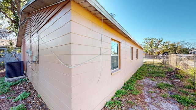 view of side of home with concrete block siding, central AC unit, and fence