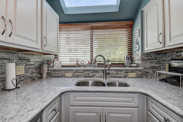 1500 Sunset Rd Unit G4, Tarpon Springs, FL 34689 - kitchen featuring light stone countertops, a skylight, a sink, decorative backsplash, and white cabinets