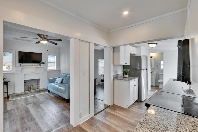 1138 Howard St, Clearwater, FL 33756 - kitchen featuring white cabinets, freestanding refrigerator, a brick fireplace, and light wood finished floors