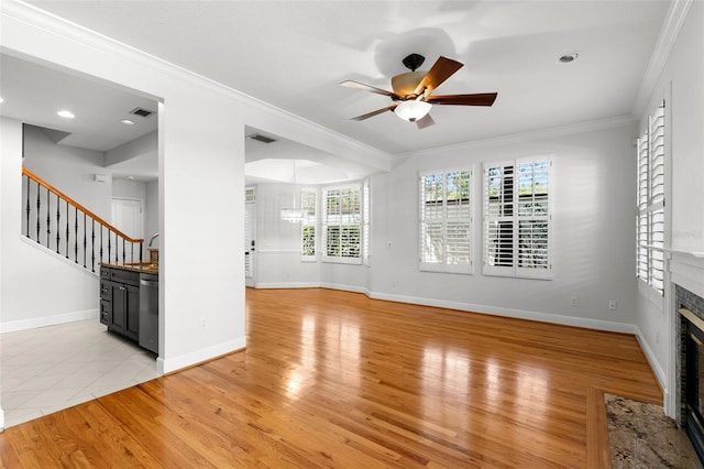 unfurnished living room with crown molding, a fireplace with flush hearth, light wood-type flooring, a ceiling fan, and stairs