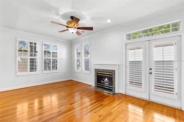 unfurnished living room featuring baseboards, a ceiling fan, crown molding, a high end fireplace, and wood finished floors