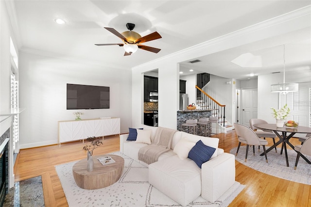 living room featuring crown molding, a fireplace with flush hearth, visible vents, stairway, and baseboards