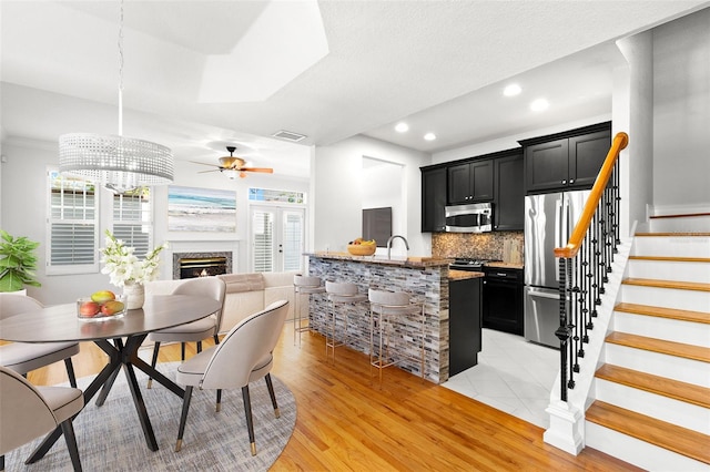 dining area with light wood-style floors, visible vents, recessed lighting, stairway, and a premium fireplace