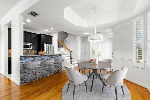 dining room featuring light wood-style floors, an inviting chandelier, visible vents, stairs, and baseboards