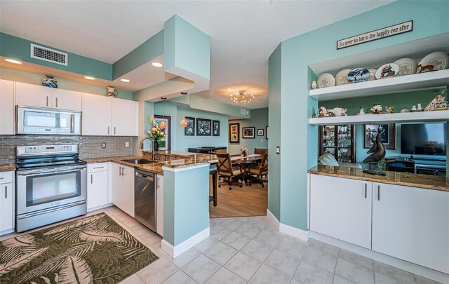 4801 Osprey Dr S Unit 508, Saint Petersburg, FL 33711 - kitchen with visible vents, a peninsula, dark stone counters, stainless steel appliances, and white cabinetry