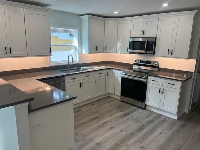 kitchen featuring a sink, stainless steel appliances, dark countertops, and light wood finished floors