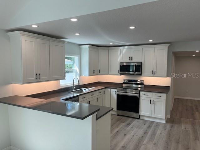 kitchen with stainless steel appliances, recessed lighting, dark countertops, a sink, and light wood-type flooring