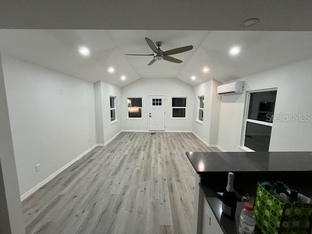 unfurnished living room with a wall mounted AC, baseboards, ceiling fan, lofted ceiling, and light wood-style floors