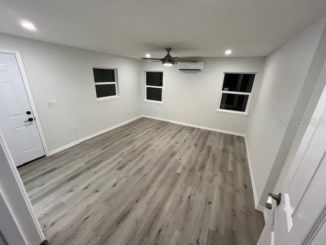 empty room featuring a wall unit AC, recessed lighting, baseboards, a ceiling fan, and wood finished floors