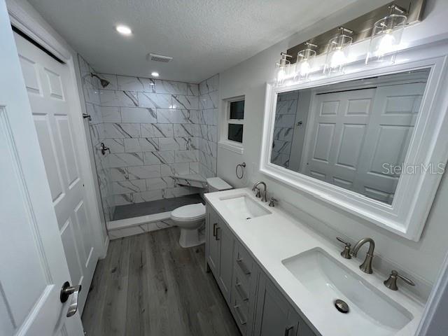 full bath with visible vents, a sink, double vanity, and tiled shower