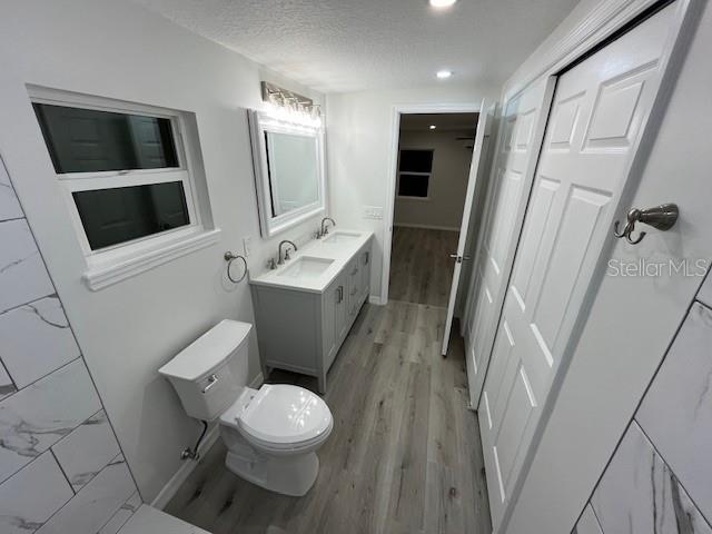 bathroom with a textured ceiling, toilet, wood finished floors, recessed lighting, and a sink