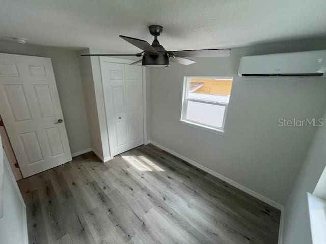unfurnished bedroom with a closet, baseboards, ceiling fan, light wood-type flooring, and a wall unit AC