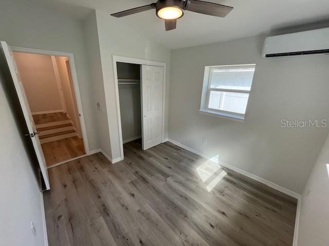 unfurnished bedroom with a wall unit AC, baseboards, a ceiling fan, a closet, and wood finished floors