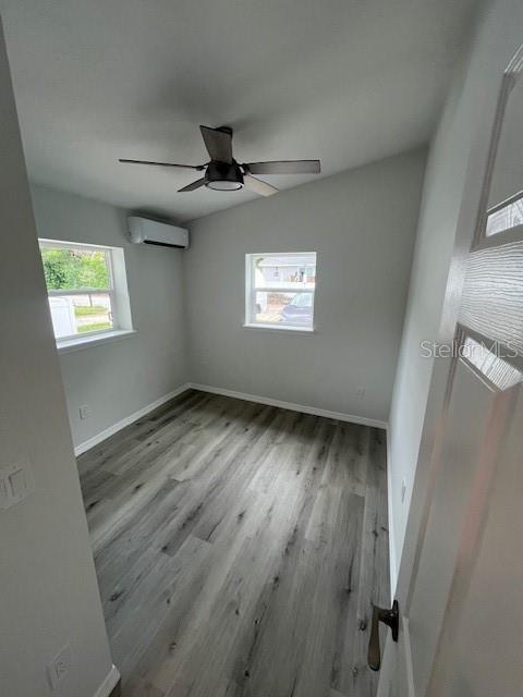 empty room with baseboards, a wall mounted AC, wood finished floors, and a ceiling fan