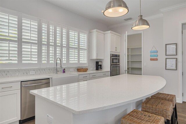 16306 1st St E, Redington Beach, FL 33708 - kitchen with white cabinets, crown molding, stainless steel appliances, a kitchen island, and a sink