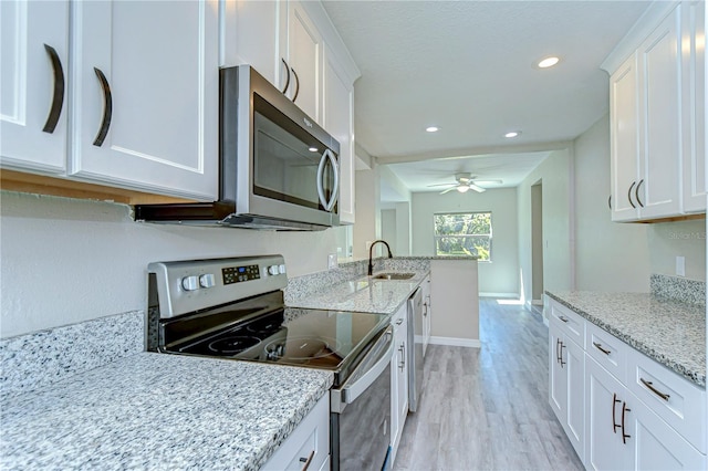 804 Shore Dr W, Oldsmar, FL 34677 - kitchen with light wood-style flooring, light stone countertops, appliances with stainless steel finishes, white cabinetry, and a sink