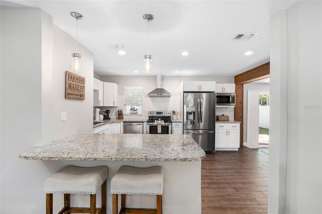 kitchen featuring wall chimney range hood, a peninsula, white cabinets, and appliances with stainless steel finishes