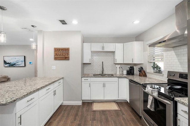 kitchen with visible vents, a peninsula, wall chimney exhaust hood, a sink, and stainless steel appliances