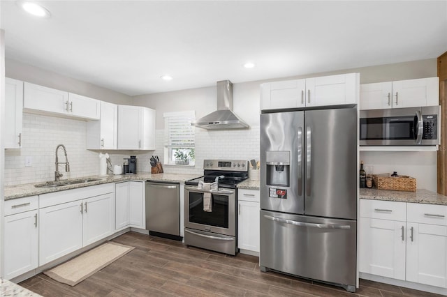 kitchen featuring appliances with stainless steel finishes, dark wood finished floors, white cabinetry, a sink, and wall chimney exhaust hood