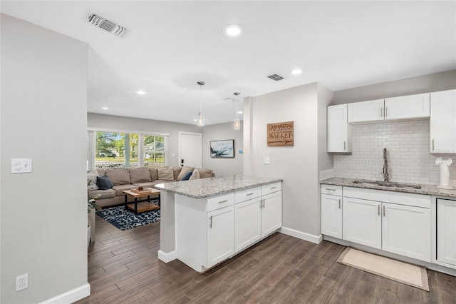 kitchen with visible vents, a peninsula, baseboards, white cabinetry, and a sink