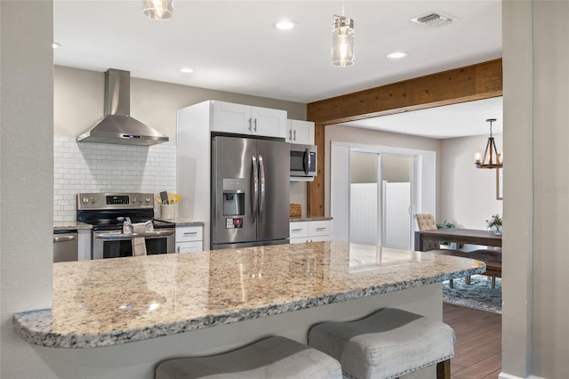 kitchen featuring wall chimney range hood, appliances with stainless steel finishes, white cabinetry, decorative backsplash, and wood finished floors