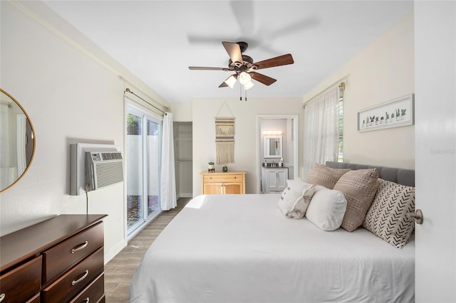 bedroom with a wall unit AC, a ceiling fan, wood finished floors, baseboards, and ensuite bathroom